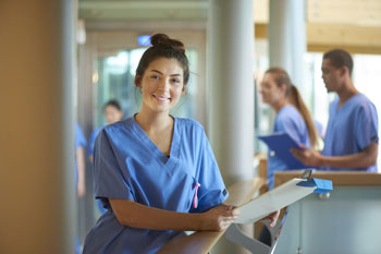 Pflegestudentin steht lächelnd in einem Krankenhausflur