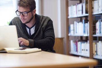 Ein Student lernt für sein Fernstudium am Schreibtisch vor einer Bücherwand.