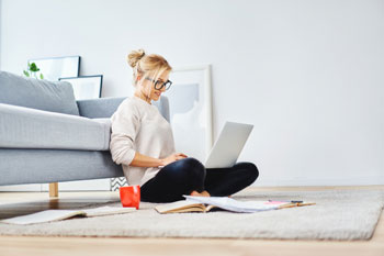 Eine Fernstudentin für Gesundheitswissenschaft sitzt auf dem Boden ihres Wohnzimmers und sieht sich ein Webinar an