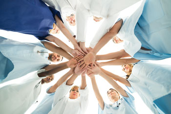 Pflegestudenten stehen im Kreis und halten jeweils eine Hand in die Mitte