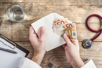 Ein Arzt nimmt mehrere Fünfzig Euro Scheine aus einem Umschlag