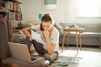 Junge Frau sitzt mit einem Laptop und Unterlagen auf dem Boden, um sich über Wartesemester zu informieren