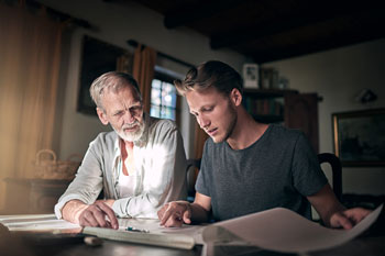 Vater und Sohn sitzen am Schreibtisch und sprechen über die Studienfinanzierung