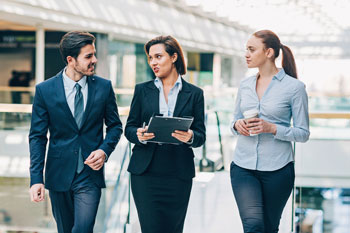 Studium Duales Studium Zwei Kolleginnen laufen mit dem dualen Studenten durch ein Unternehmen.