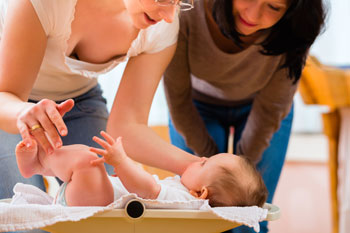 Mutter und Hebamme beugen sich liebevoll kümmernd über ein Baby