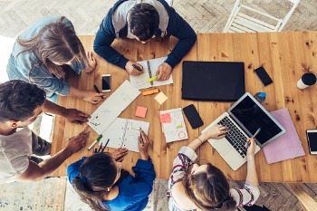 Pädagogin sitzt mit Schülern am Tisch und erarbeiten Konzepte