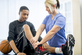 Eine Sportmedizinerin untersucht einen verletzten Basketballspieler am rechten Knie