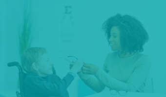 Afroamerikanische Frau reicht einem Jungen mit physischer Behinderung der im Rollstuhl sitzt seine Brille